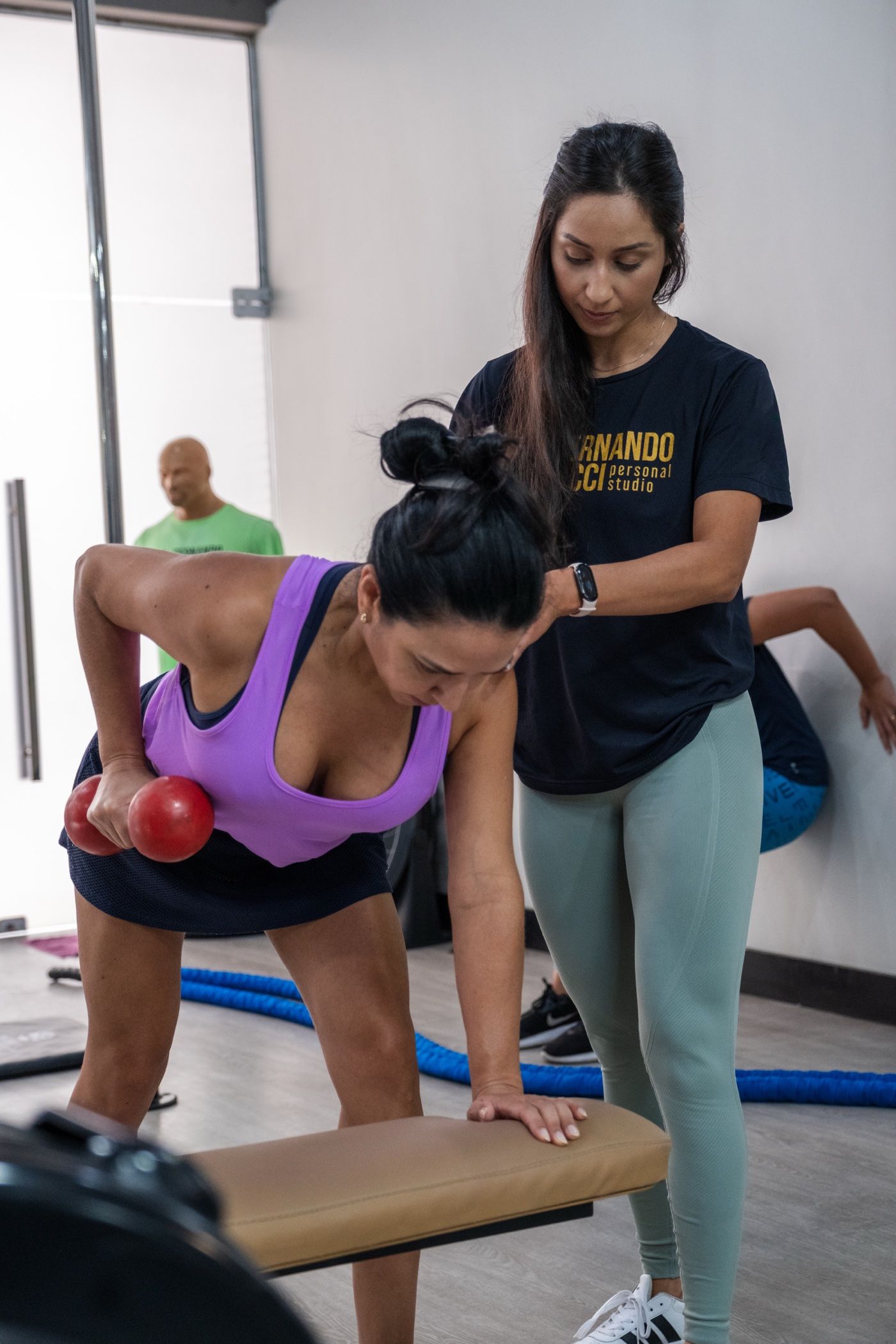 Professora orientando uma aluna no exercício com halteres