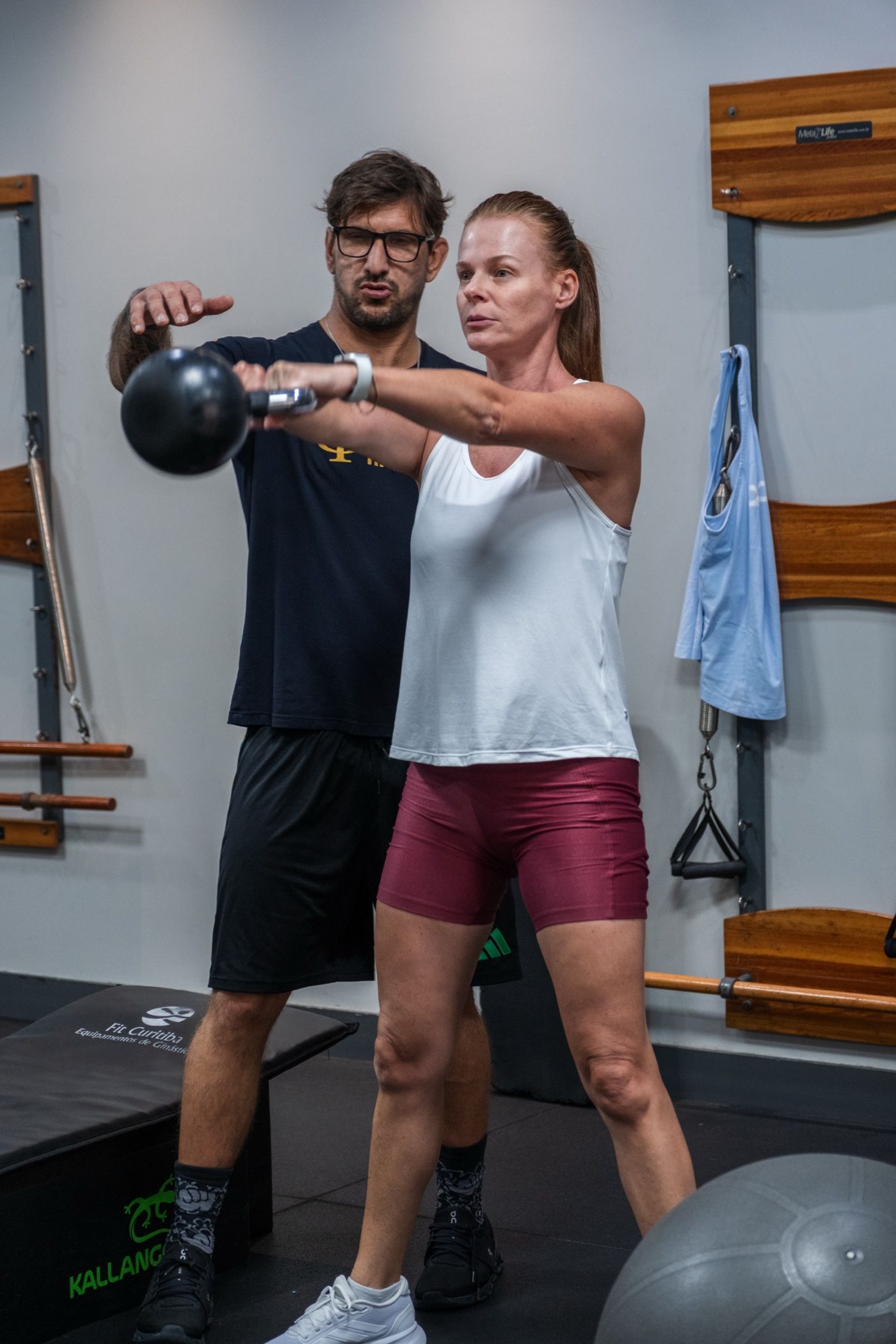 Aluna fazendo swing de kettlebell com o professor ao lado